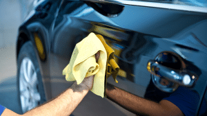 A man with a yellow cloth polishing a car