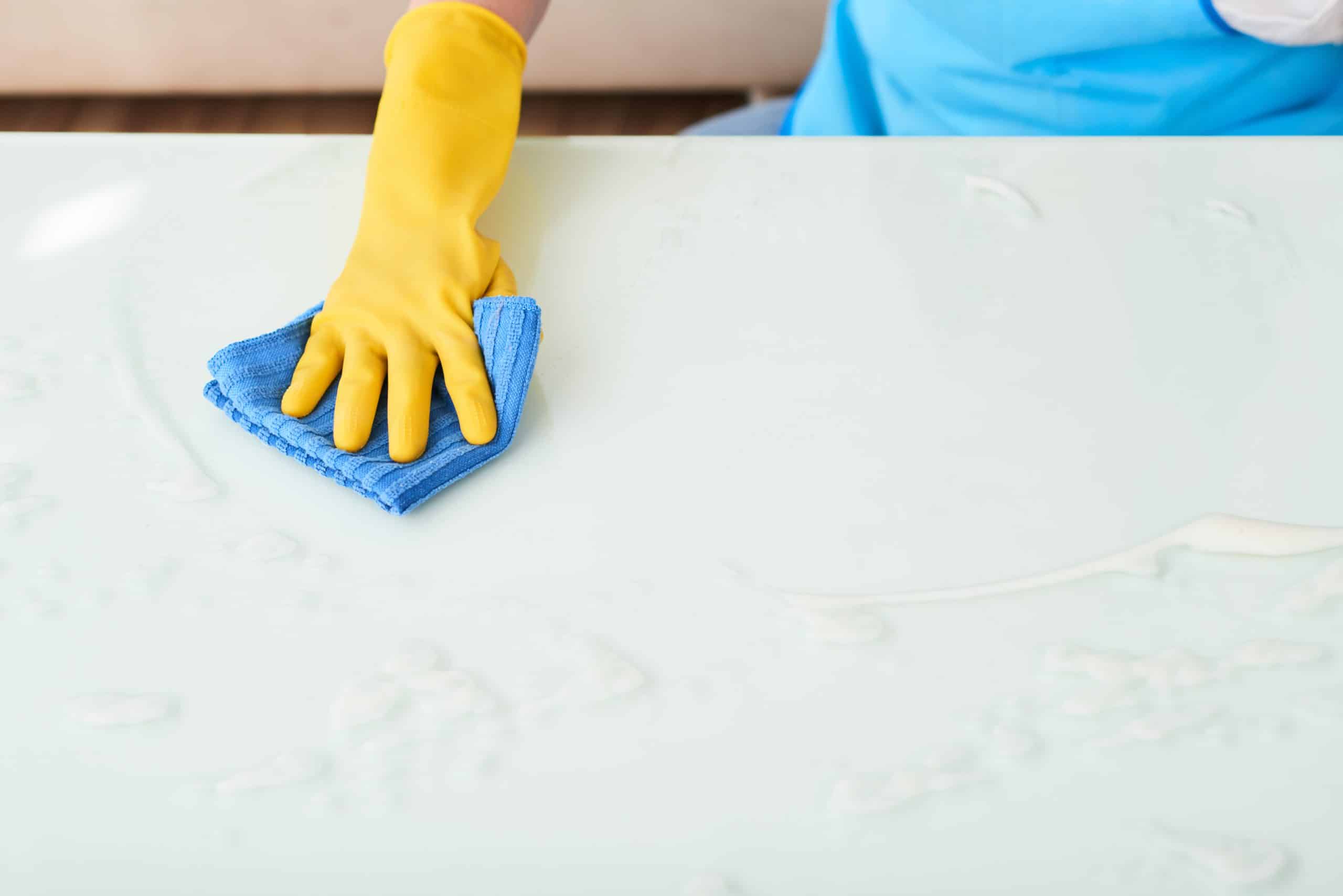 Gloved hand on woman cleaning white surface of table