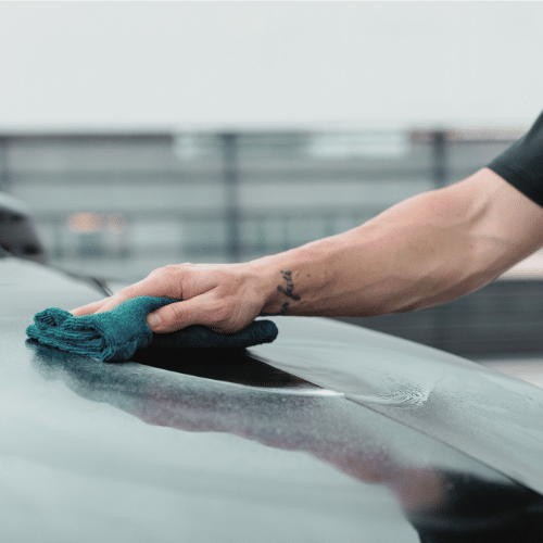 A person using a blue cloth to clean a car
