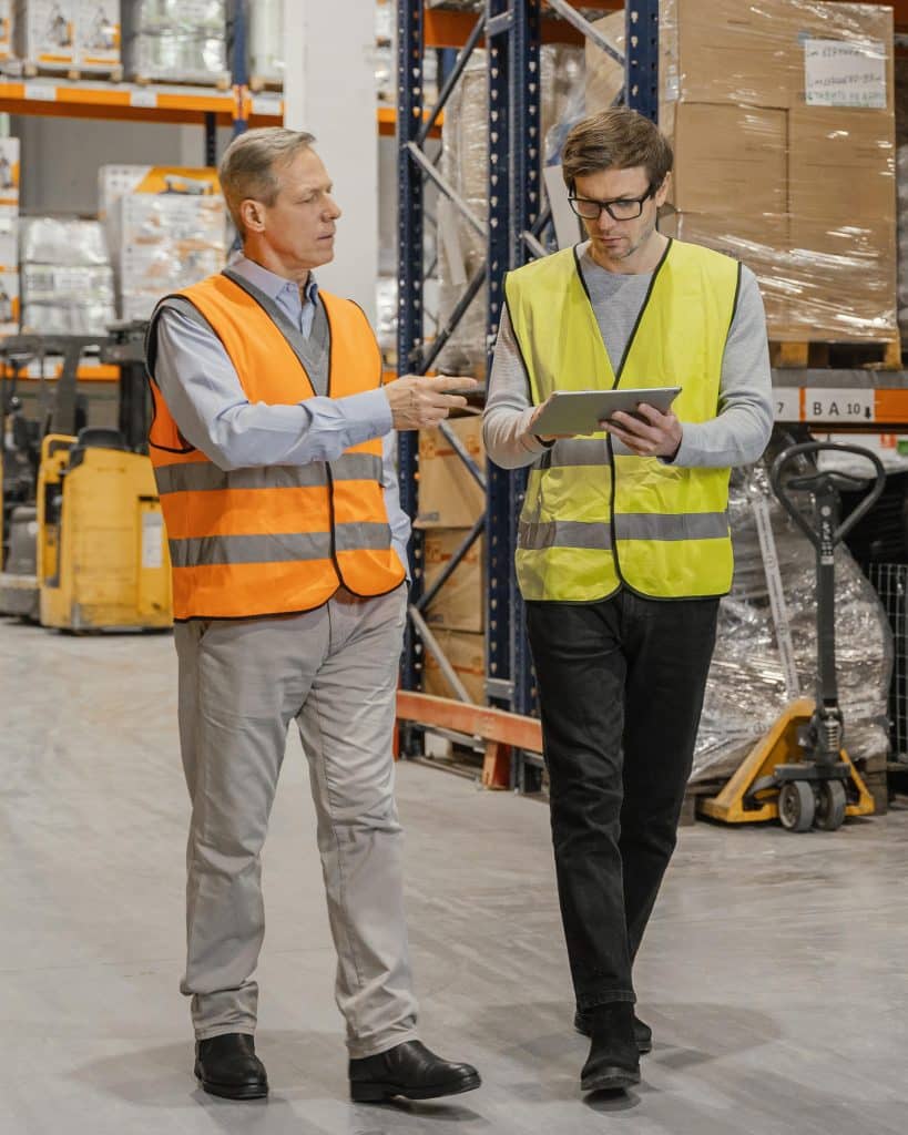 Two men in safety vests standing in a warehouse, possibly discussing work-related matters.