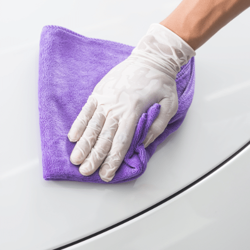 A person wearing white gloves meticulously cleans a car using a purple cloth.