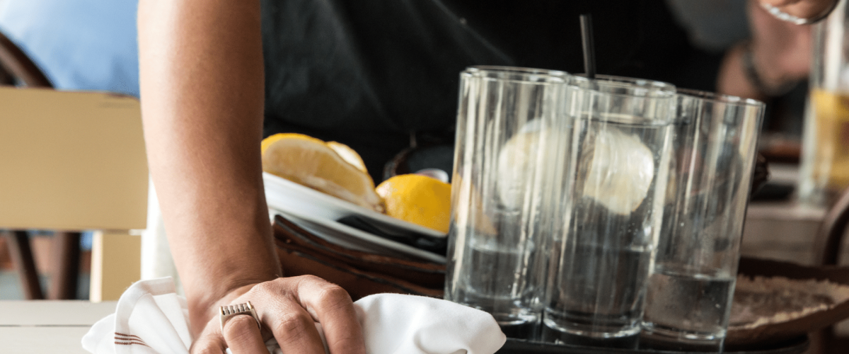 Server cleaning table with white cloth, holding tray of dishes