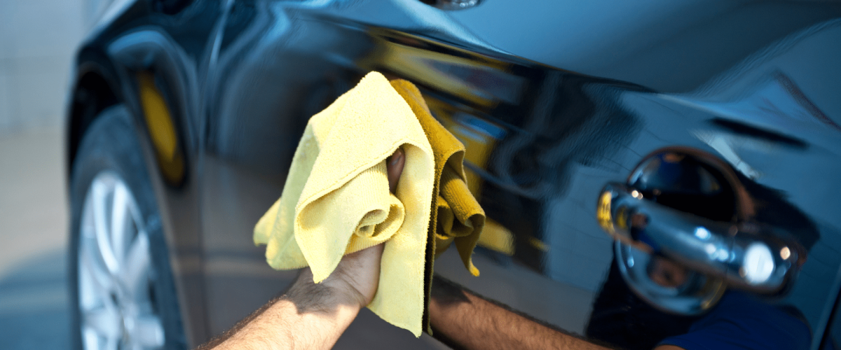 A man with a yellow cloth polishing a car